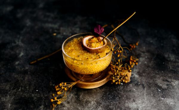 Glass dish of passion fruit tapioca pudding topped with a halved passion fruit and micro herbs.